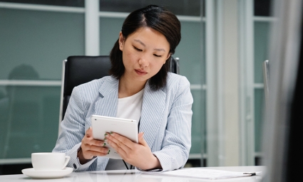 A seated business woman with a coffee reads and ipad.